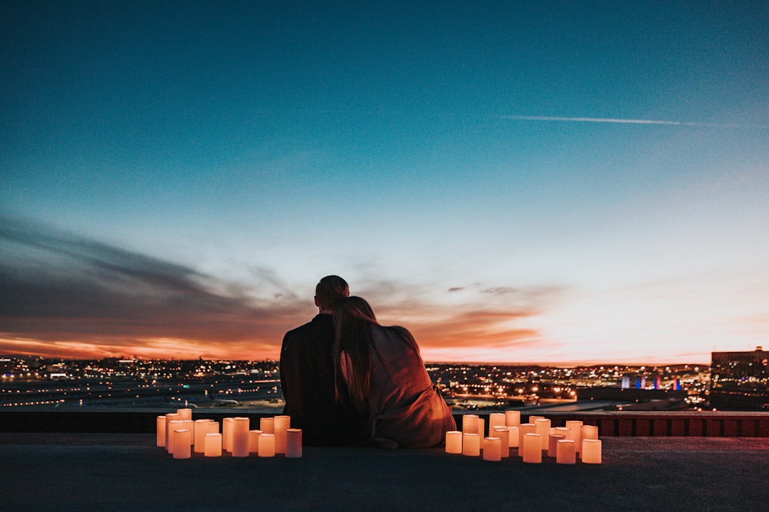 Paar sitzt auf einem Feld mit Blick auf die Stadt bei Sonnenuntergang